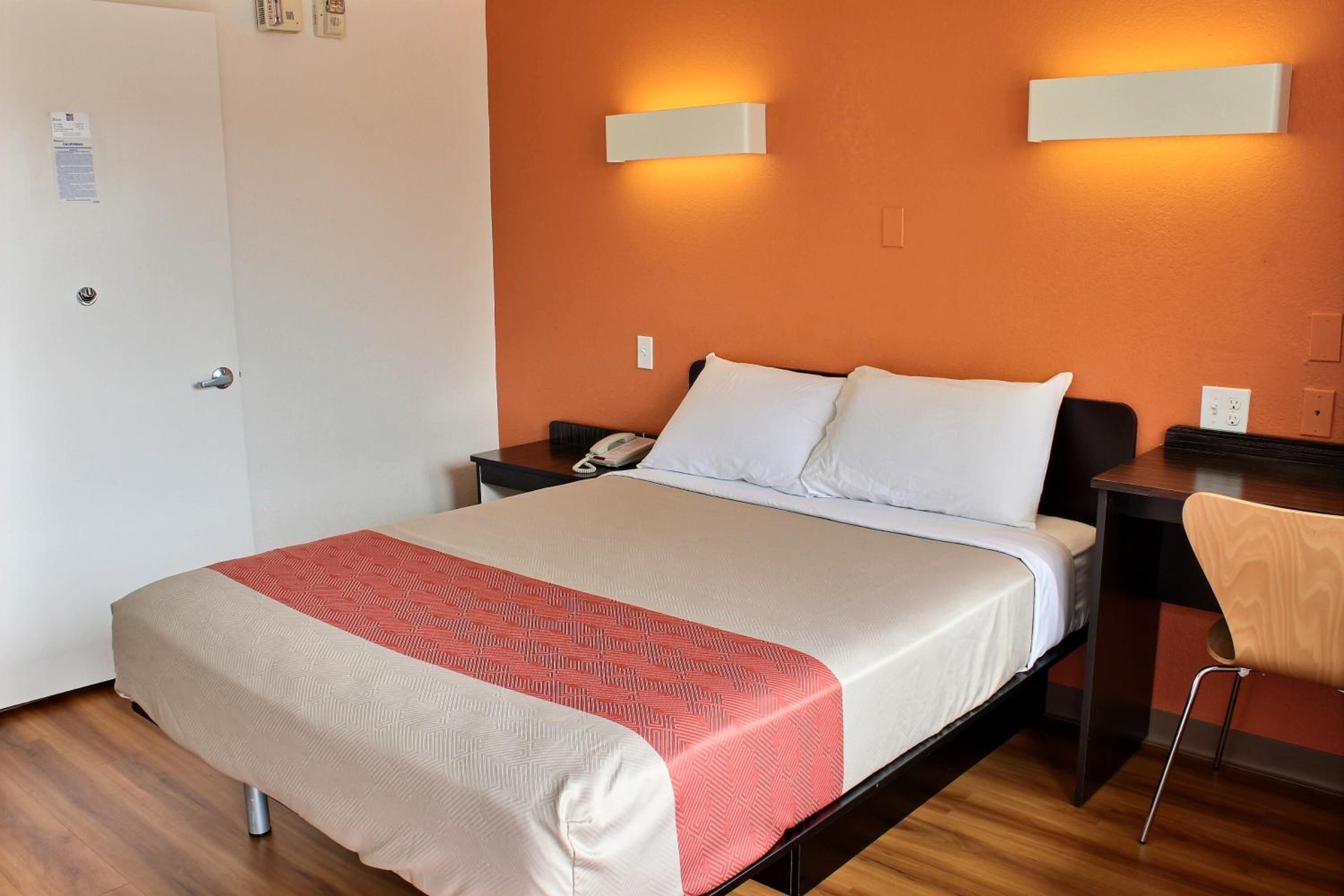 A hotel room with a bed, a desk, a chair, and two wall-mounted light fixtures.