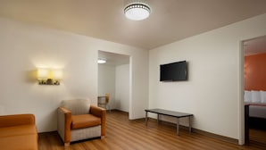 Ein modernes Zimmer mit Holzboden, einer Couch, einem Sessel, einem kleinen Tisch und einem an der Wand befestigten Fernseher.