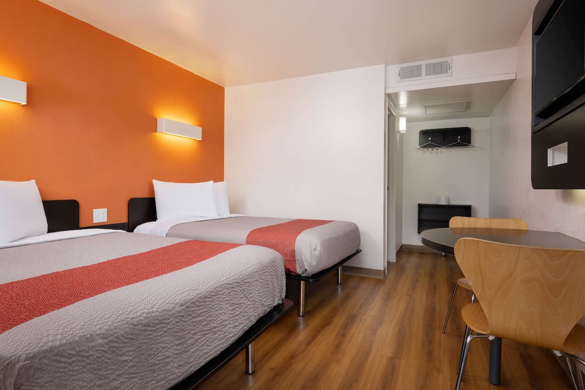 Een hotelkamer met twee bedden, een houten eettafel en een aan de muur bevestigde televisie.