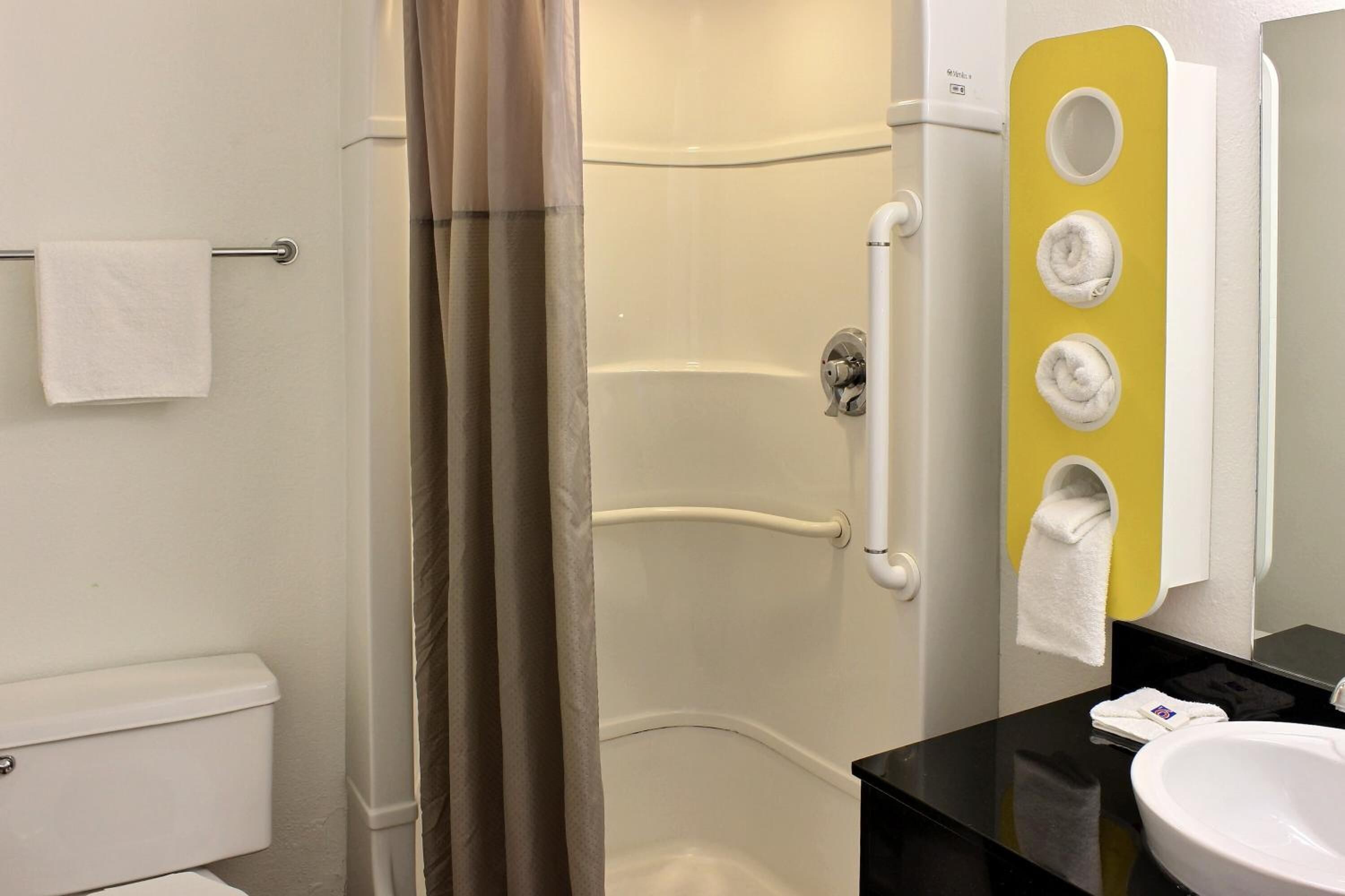 A bathroom with a shower, toilet, and sink. There are towels hanging on a rack and a mirror with a yellow accent wall.
