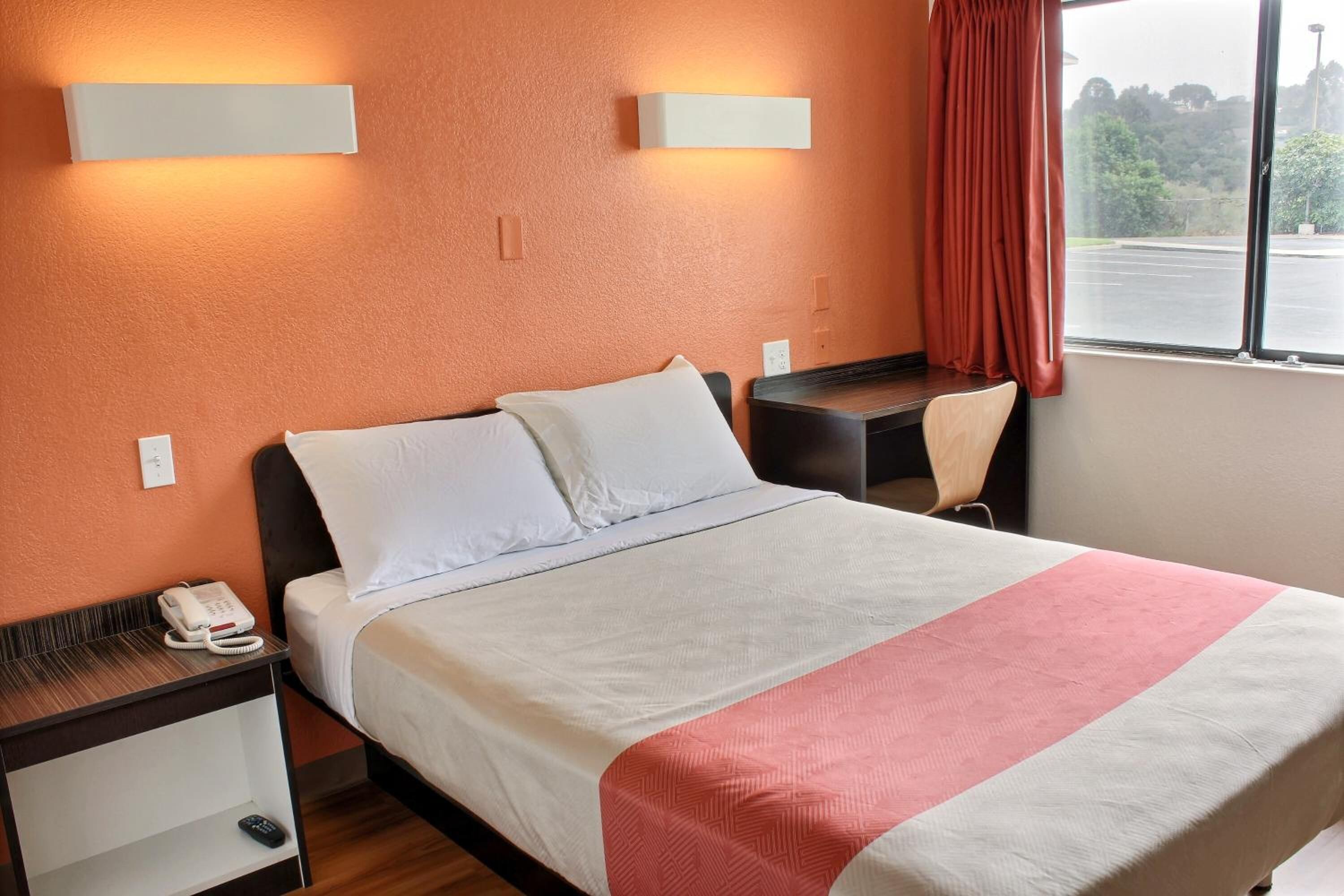 A hotel room with a bed, bedside tables, a desk, and a window with curtains.