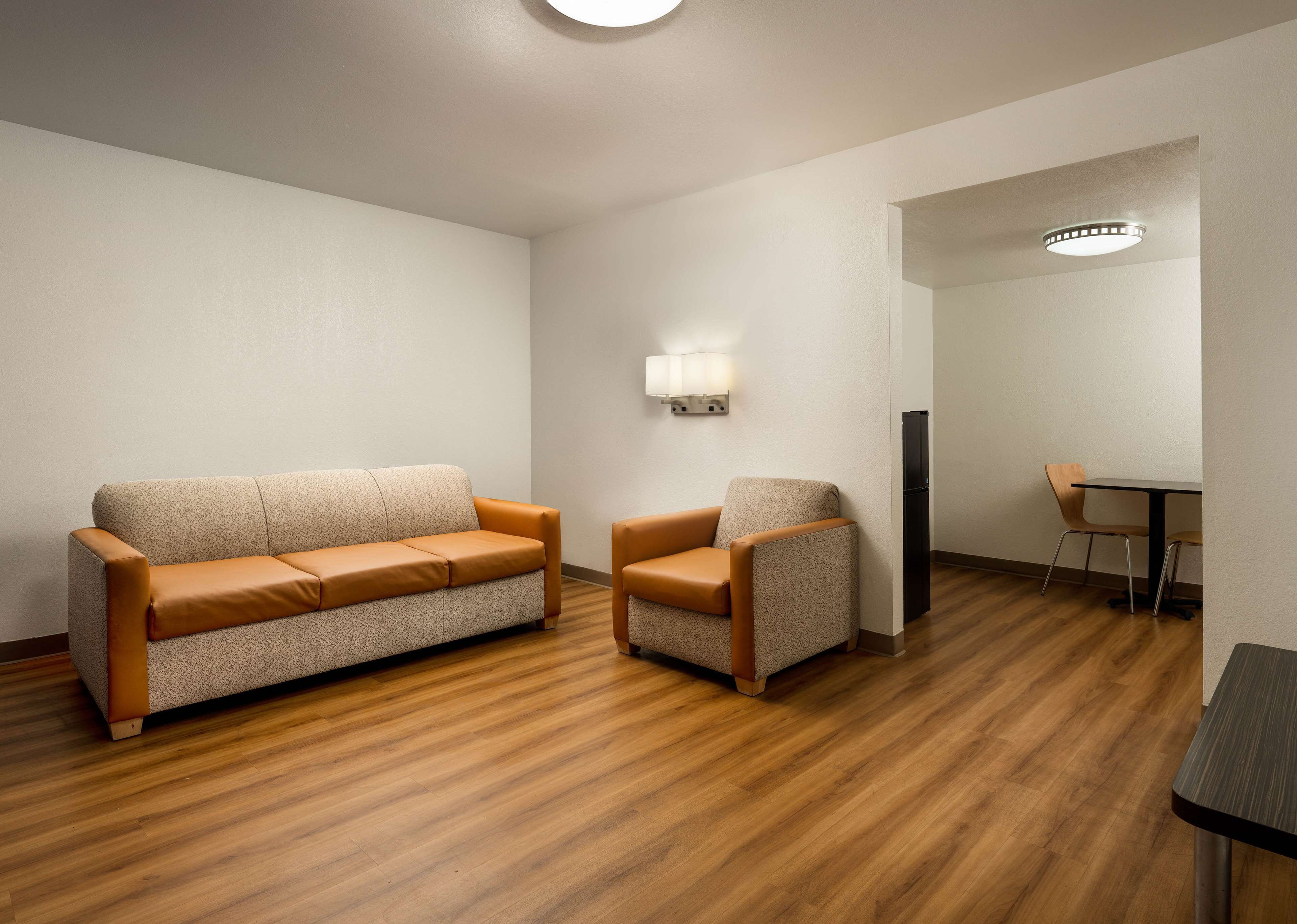 Una habitación con piso de madera, un sofá, una silla, una mesa y una lámpara.