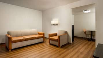 Una habitación con piso de madera, un sofá, una silla, una mesa y una lámpara.