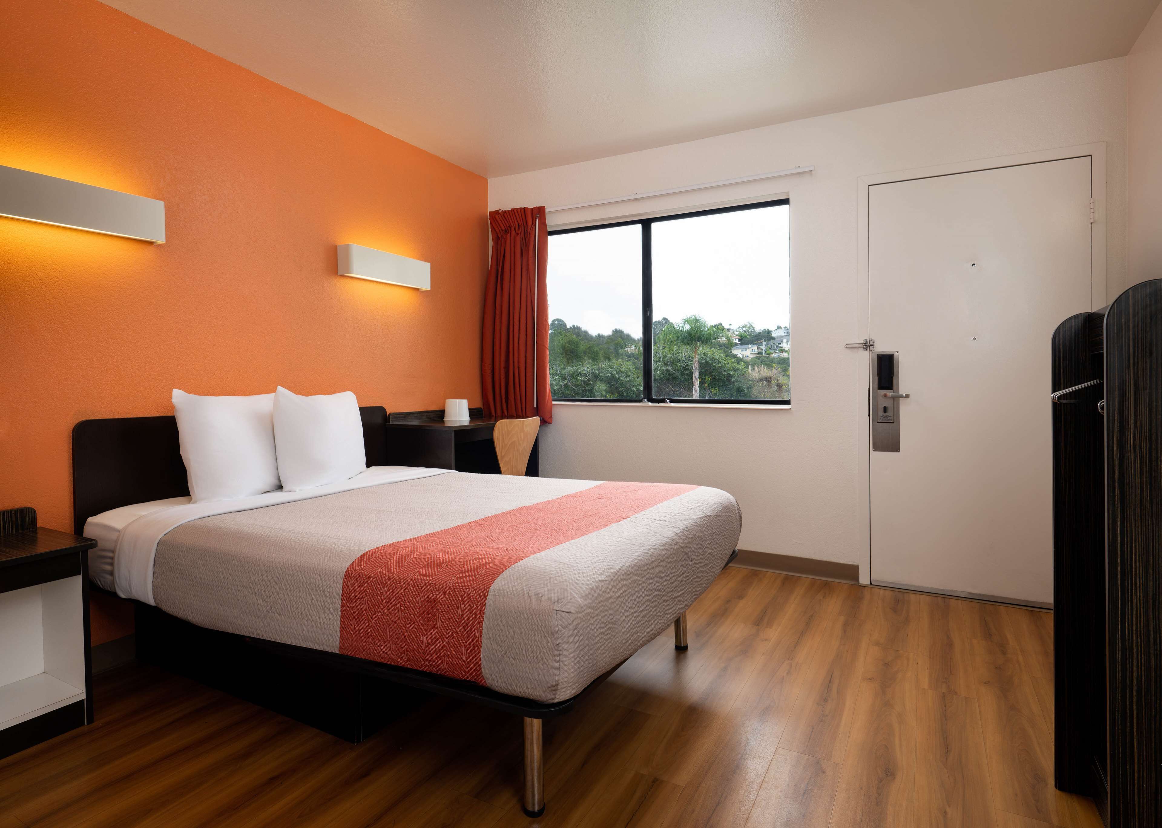 Een hotelkamer met een bed, nachtkastje, raam met gordijnen en een deur.