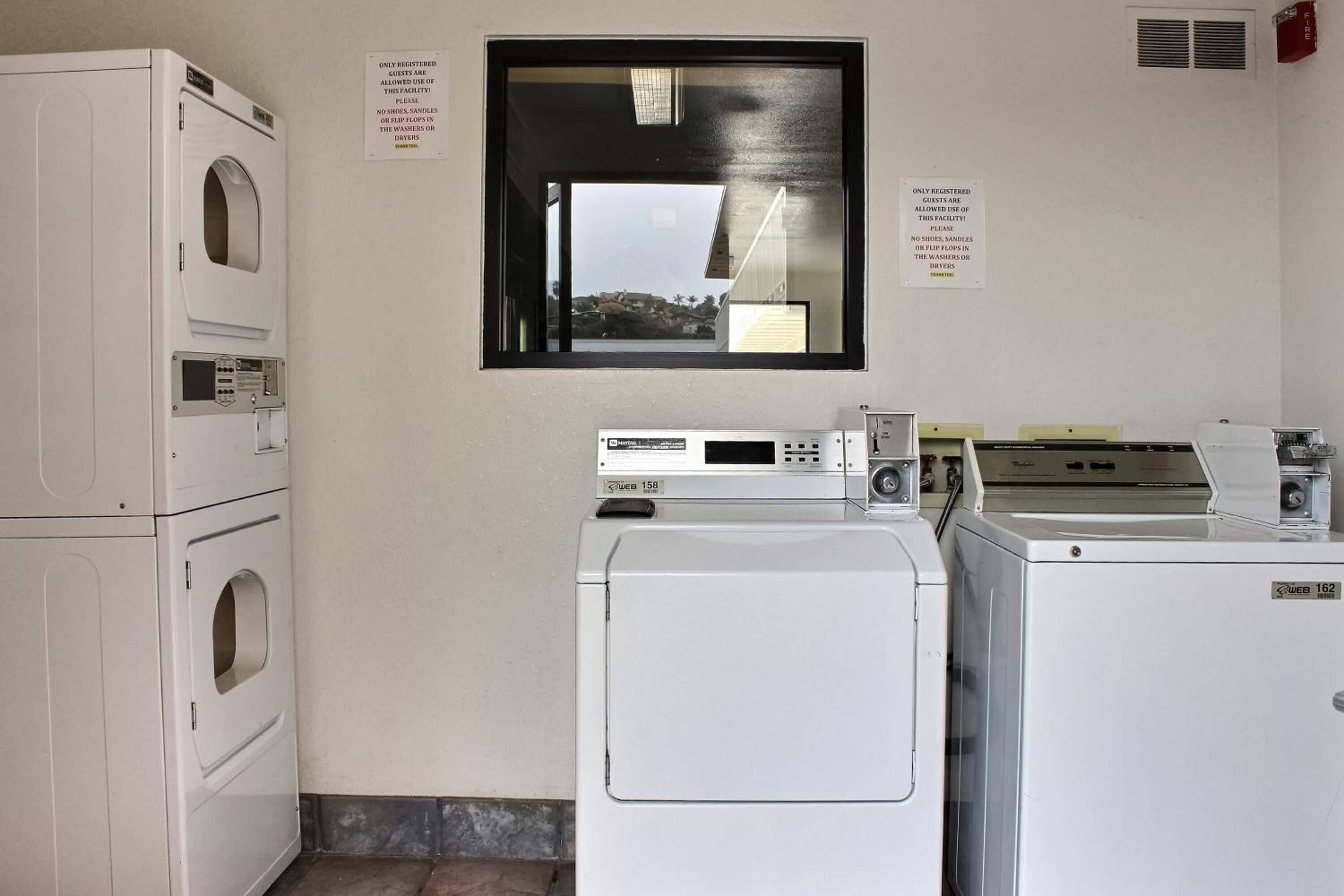 A laundry area with stacked washers and dryers, a control panel, and two signs on the wall.