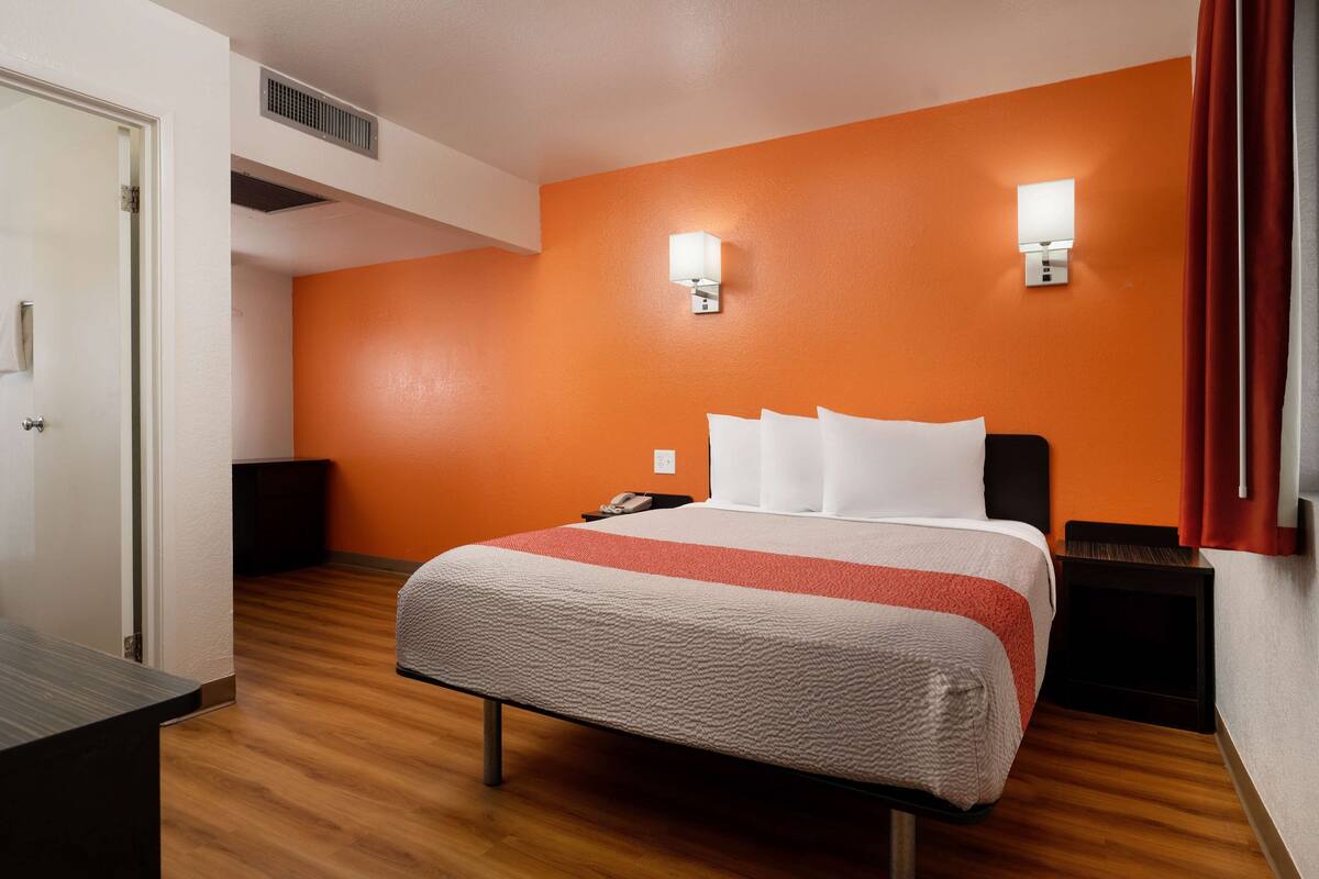 Een hotelkamer met een bed, een nachtkastje, een telefoon en een wandlamp.