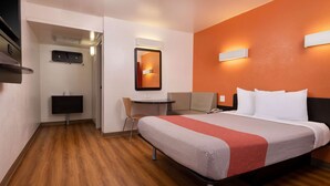 Ein Hotelzimmer mit Bett, Schreibtisch, Stuhl, Fernseher und Spiegel.