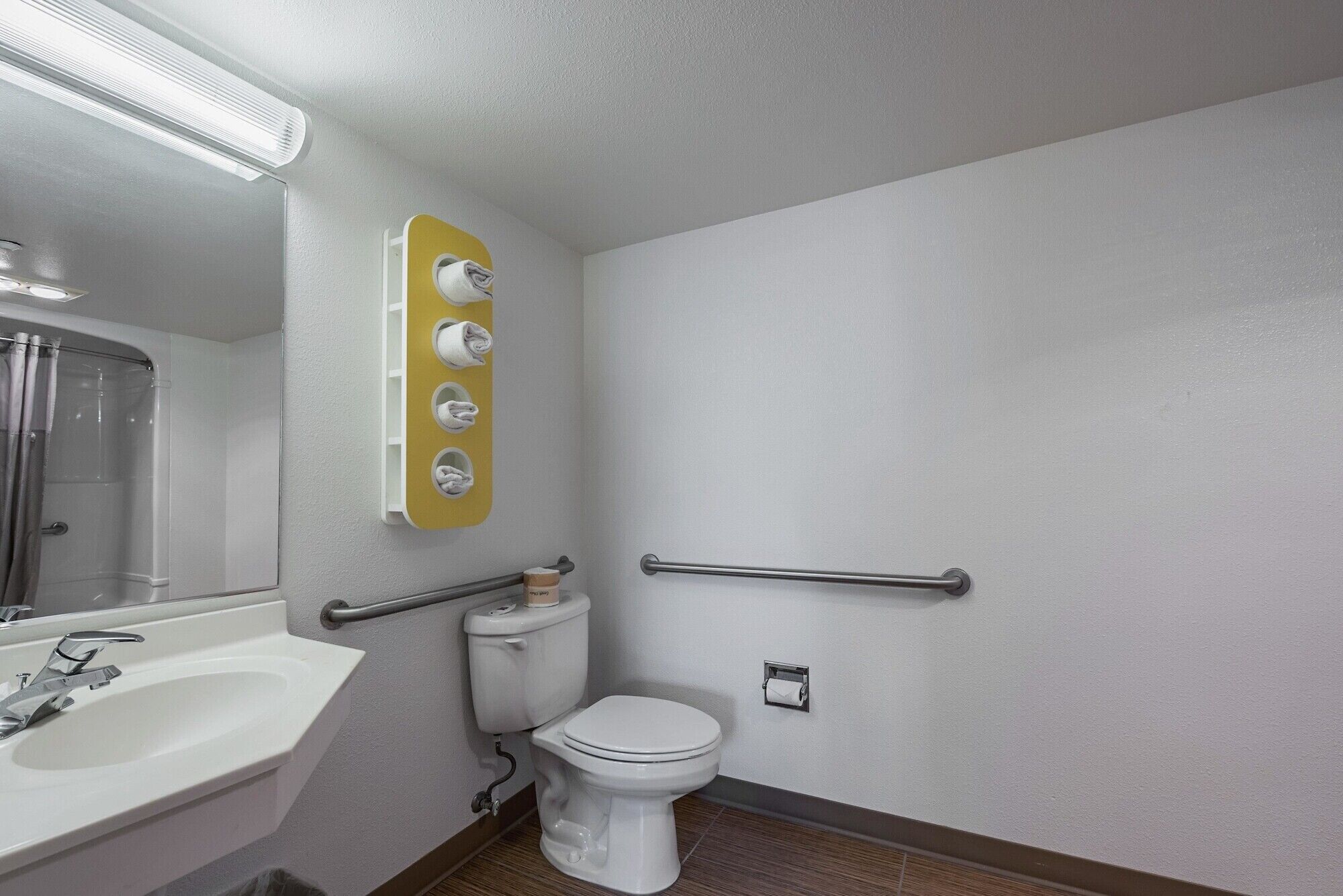 A bathroom with a white sink, a toilet, a shower, and a towel rack with four towels.