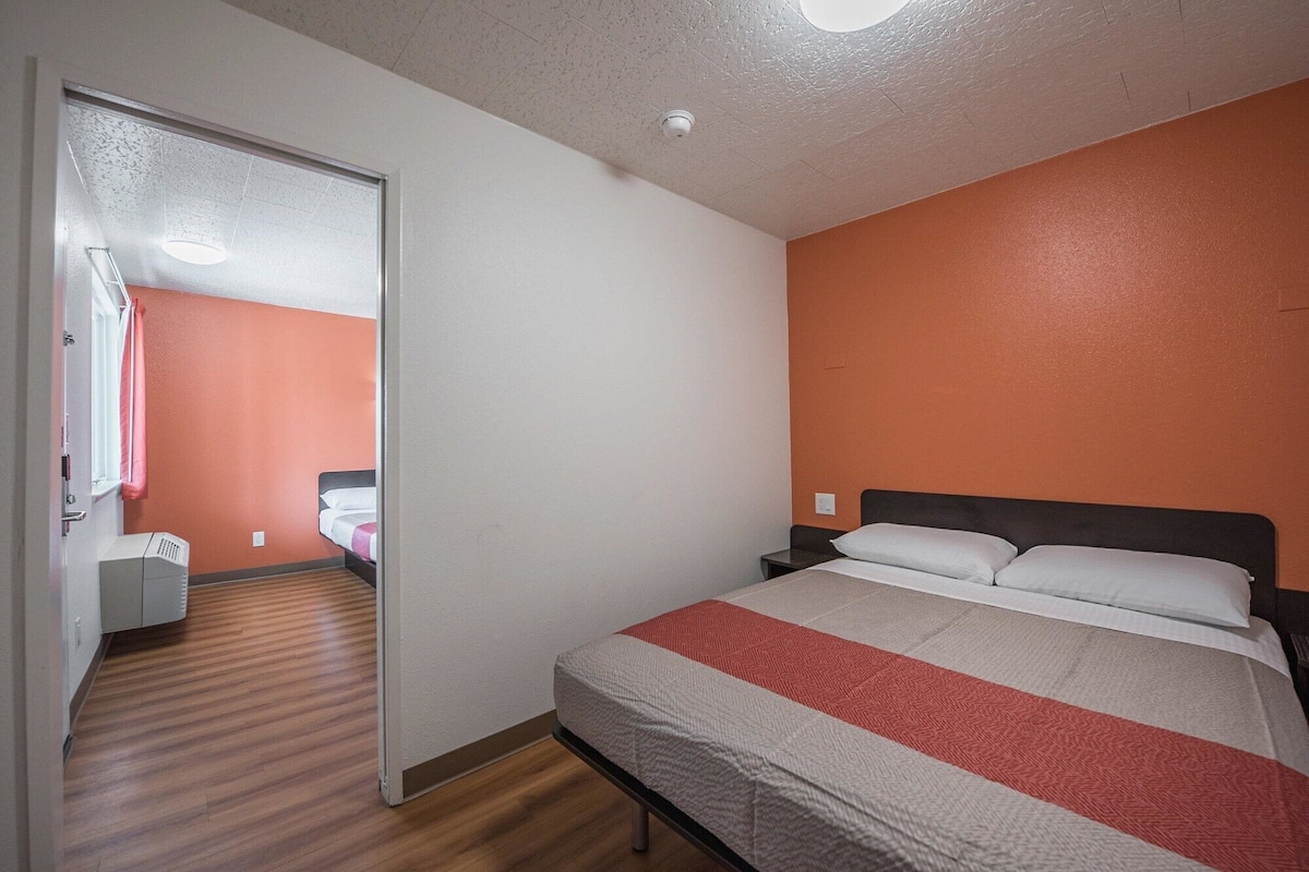 Habitación de hotel con cama, mesita de noche, escritorio y baño visible a través de una puerta abierta.