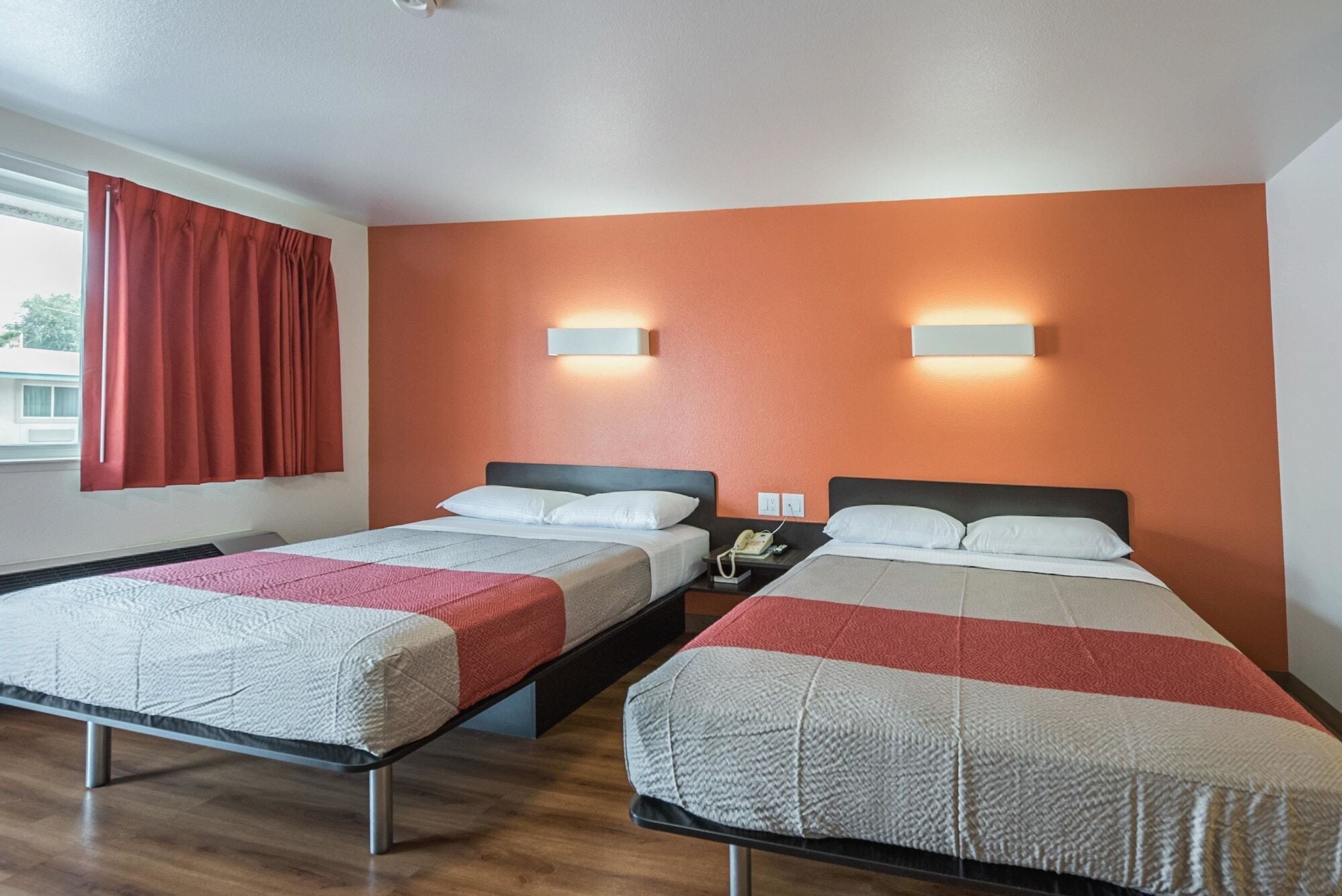 Ein Hotelzimmer mit zwei Betten, einem Fenster mit roten Vorhängen und Wandleuchten.