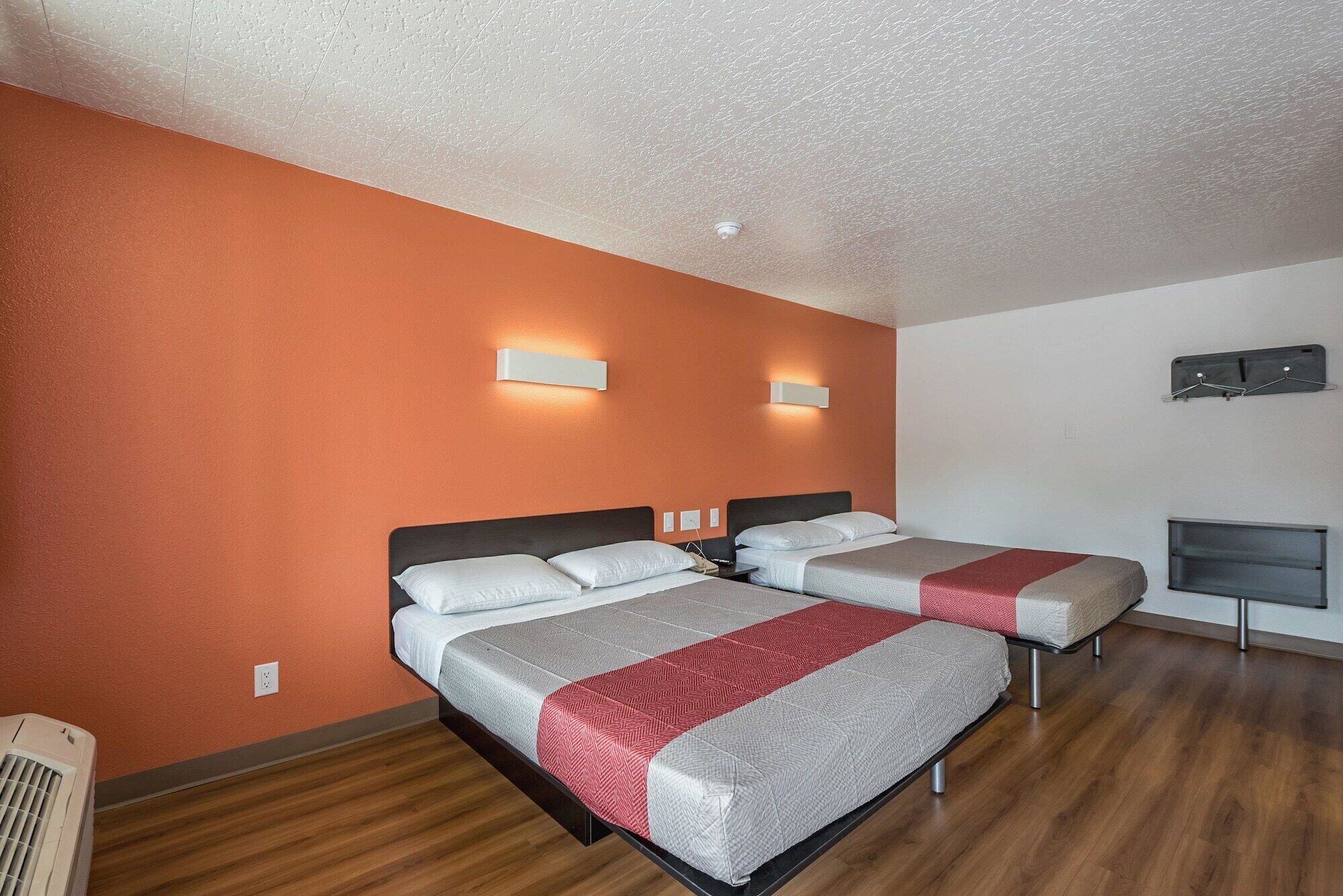 A hotel room with two beds, orange walls, and a wooden floor.