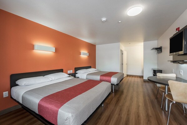 A hotel room with two beds, a desk, a chair, and a TV.