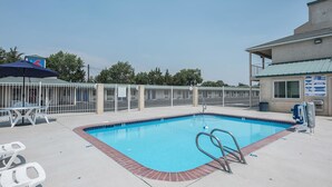 Piscina con una escalera metálica, rodeada por una valla blanca y un área de descanso cubierta con sillas.
