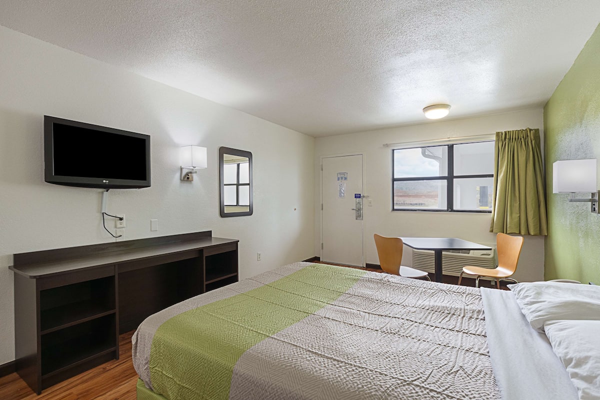 A hotel room with a bed, a desk, a chair, a television, and a window with curtains.