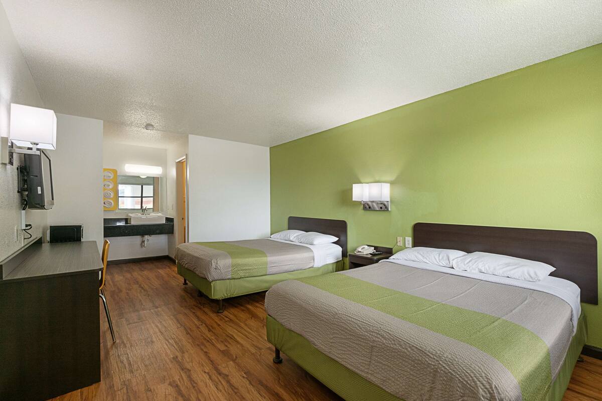 A hotel room with two beds, a desk, a chair, a sink, and a mirror.