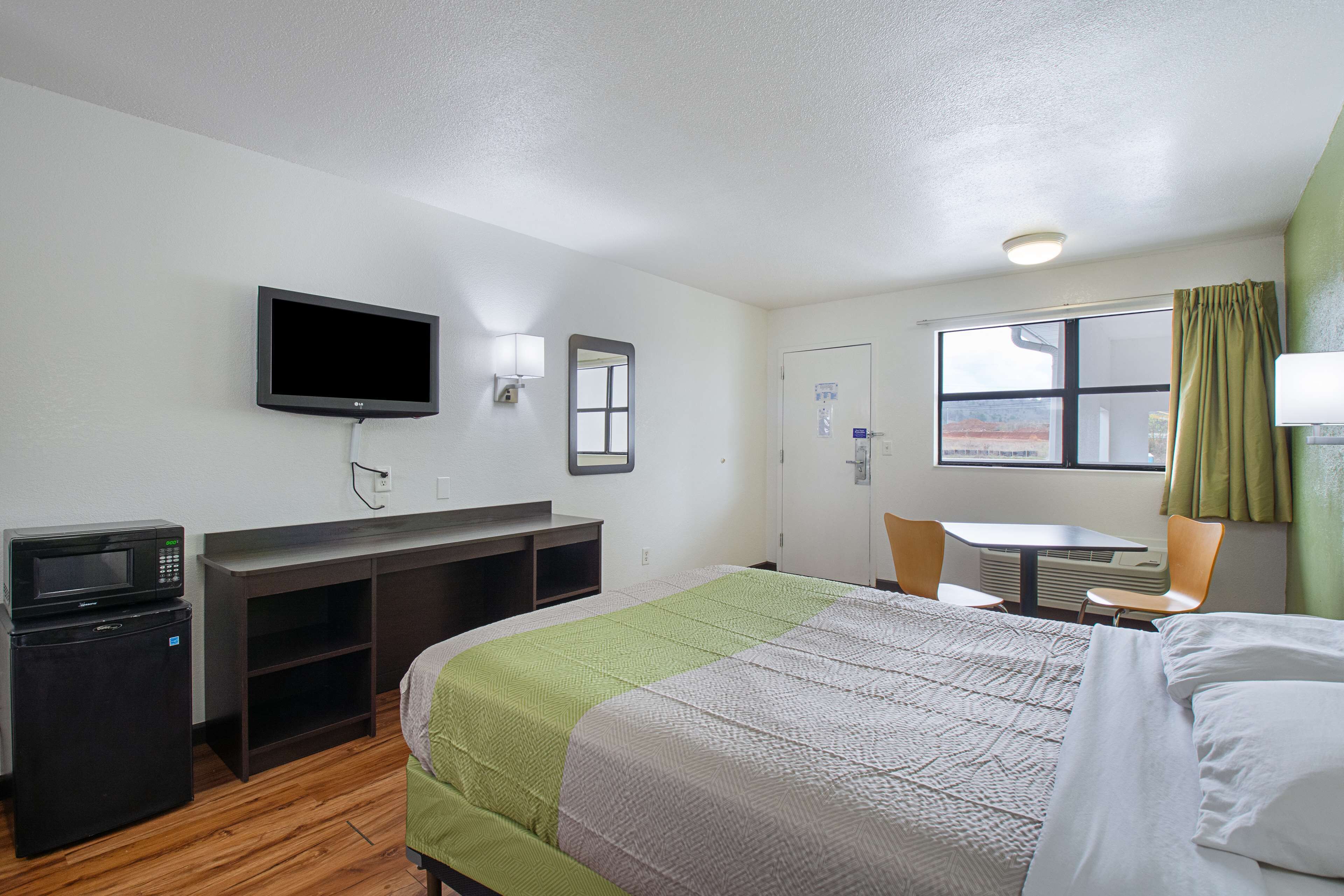 A hotel room with a bed, a desk, a television, a microwave, and a window with curtains.