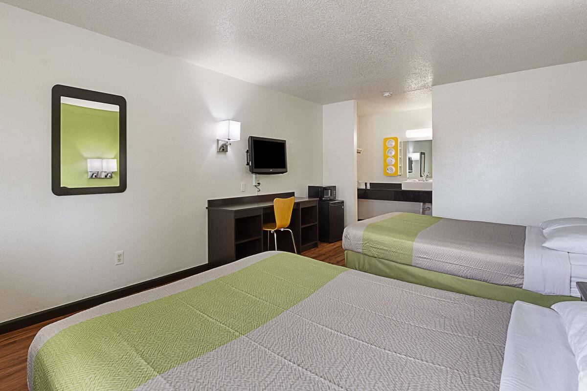 A hotel room with two beds, a desk with a chair, a television, and a mirror.
