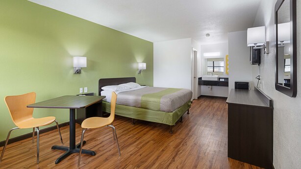 A hotel room with a bed, two chairs, a desk, a mirror, and a bathroom with a sink and mirror. - Motel 6 Chattanooga, TN (Chattanooga)