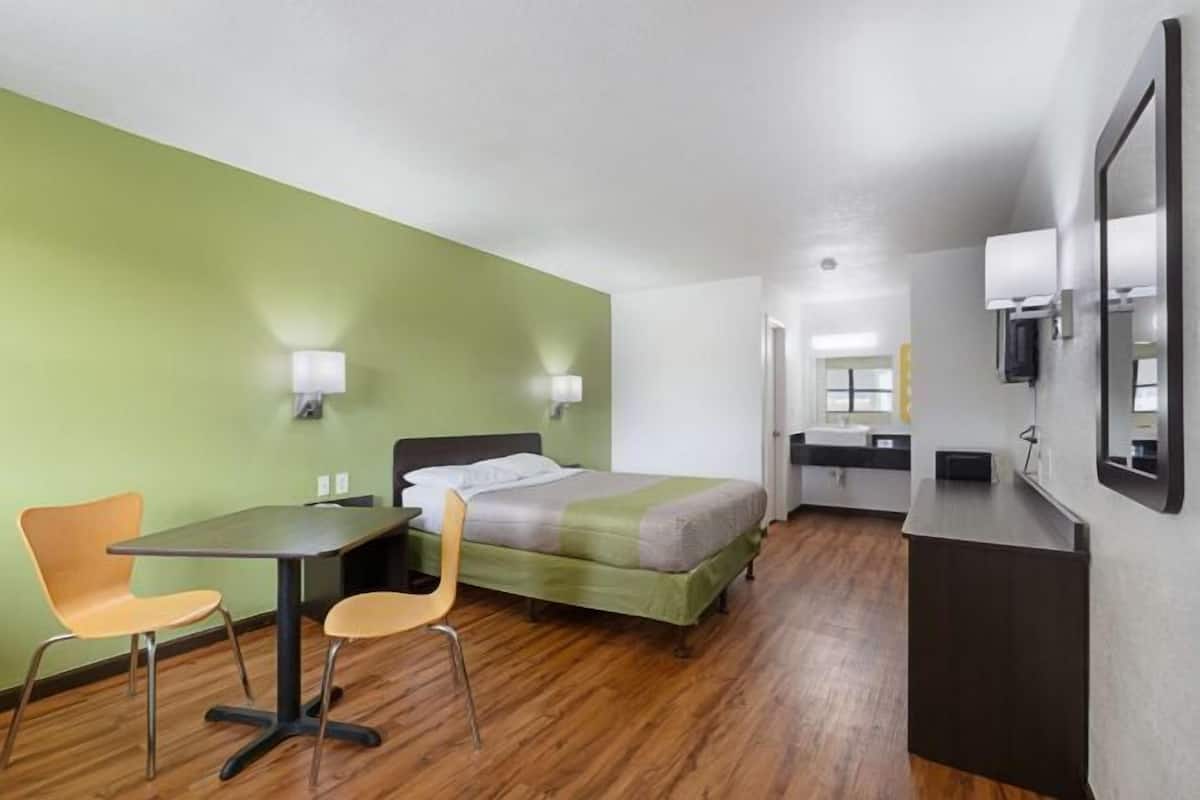 A hotel room with a bed, a desk, two chairs, a mirror, a sink, and a small kitchenette.