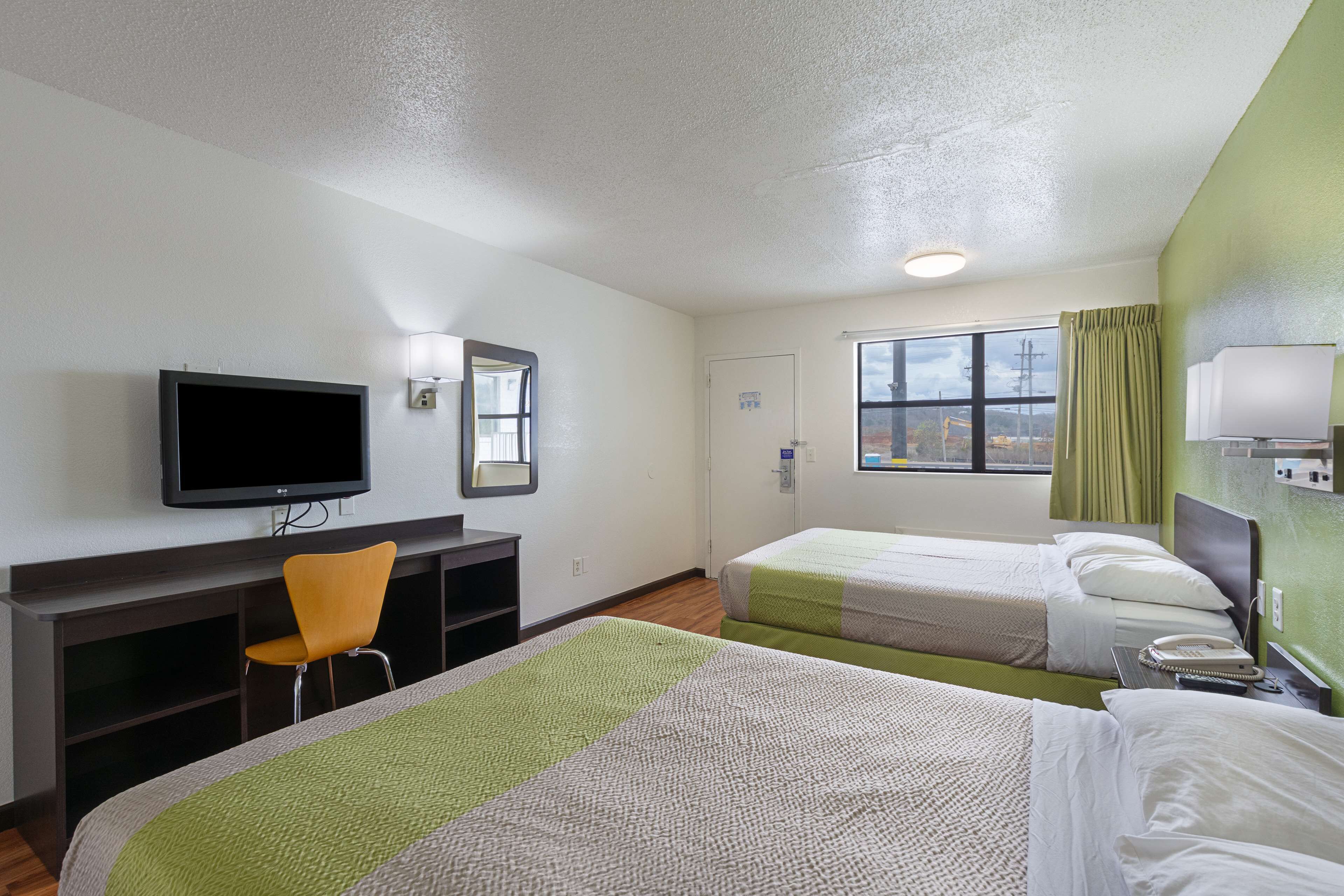 A hotel room with two beds, a TV, a desk with a chair, and a window with curtains.