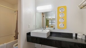A bathroom with a white sink, black countertop, and a mirror with a yellow towel rack. - Motel 6 Chattanooga, TN (Chattanooga)