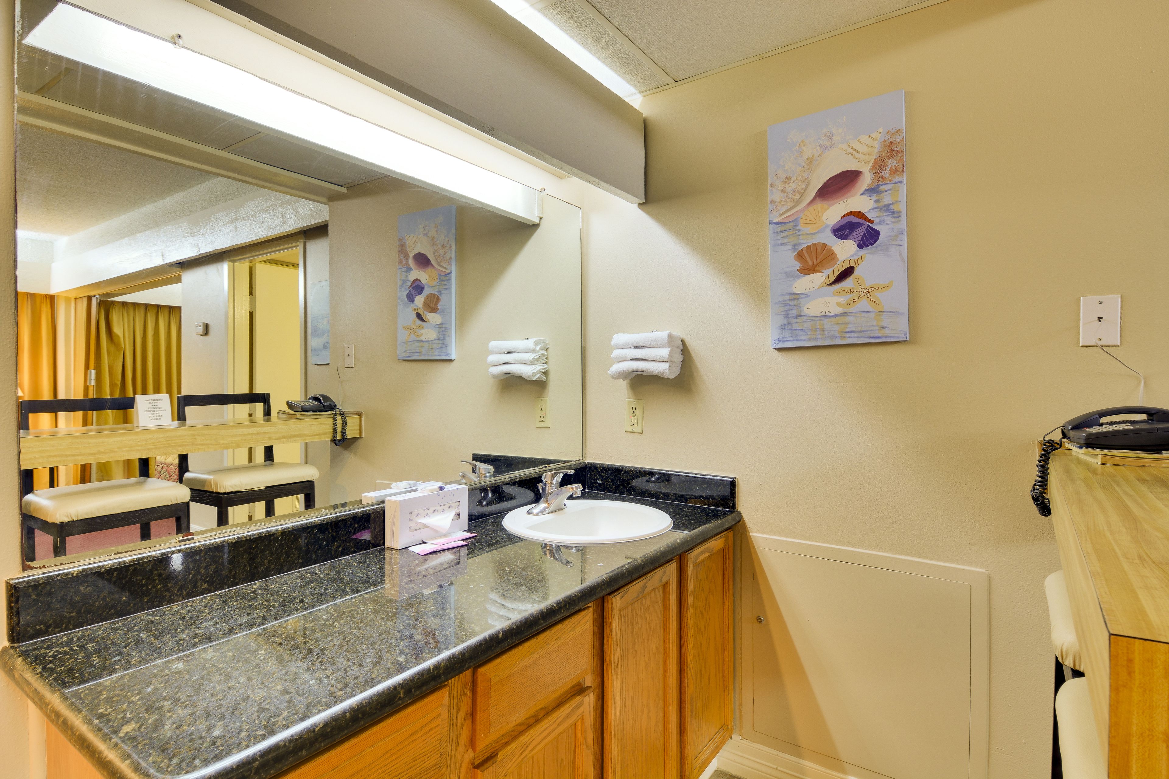 A hotel bathroom with a sink, mirror, and wooden cabinets.