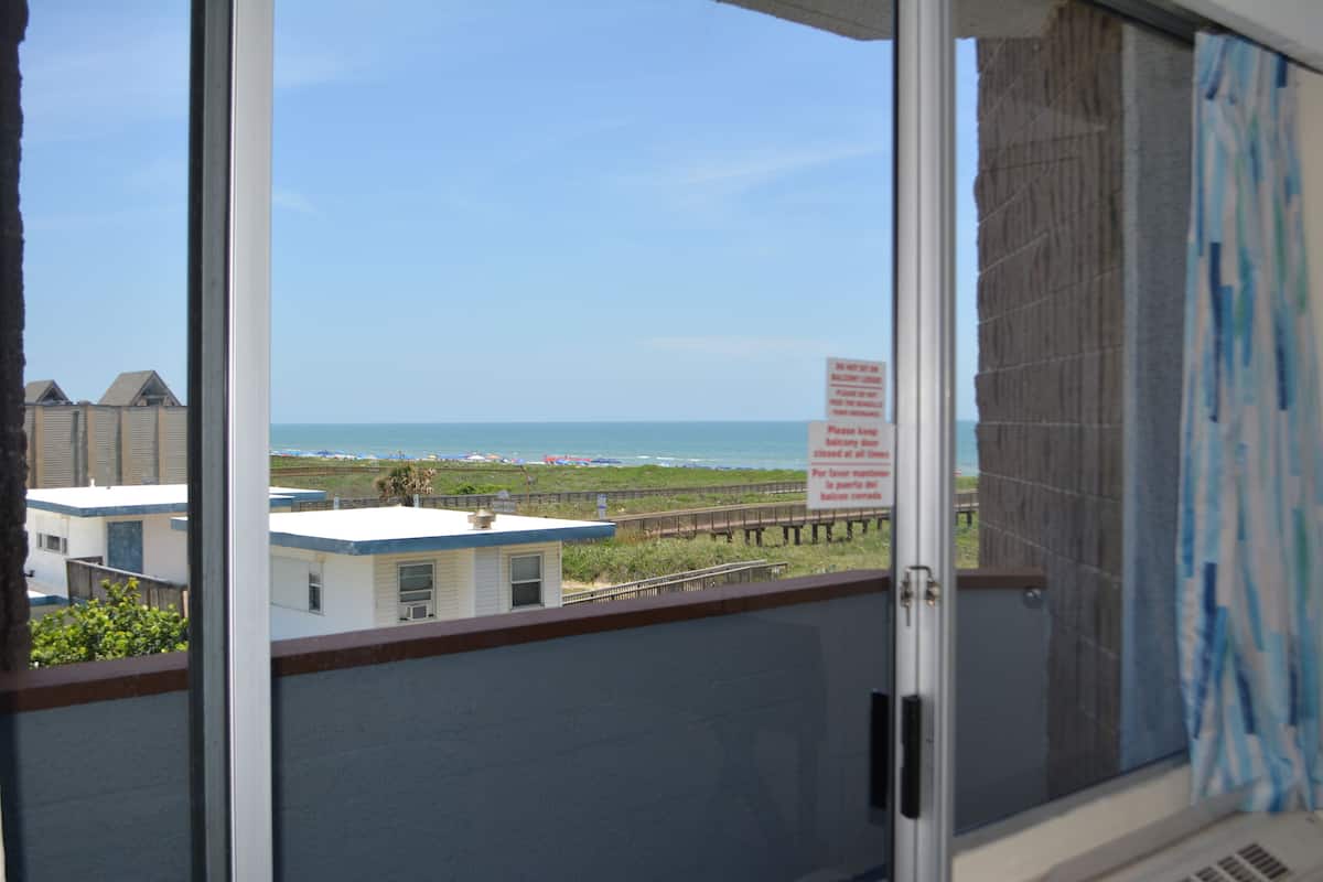 A view from a balcony overlooking a beach with a pier, a sign in a foreign language, and buildings in the background.