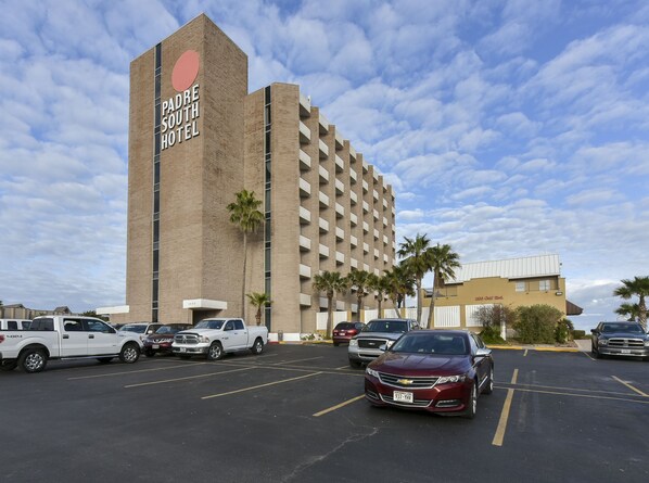 Ein Hotel mit einer großen Schilderfassade, auf der "Padre South Hotel" steht, und einem Parkplatz mit mehreren Fahrzeugen.