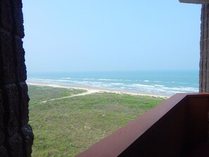 Blick auf einen Strand von einem Balkon, an einer Seite eine Steinmauer und an der anderen eine Holzbrüstung.