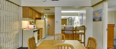 A dining area with a wooden table and chairs, a microwave, and a refrigerator in the background.