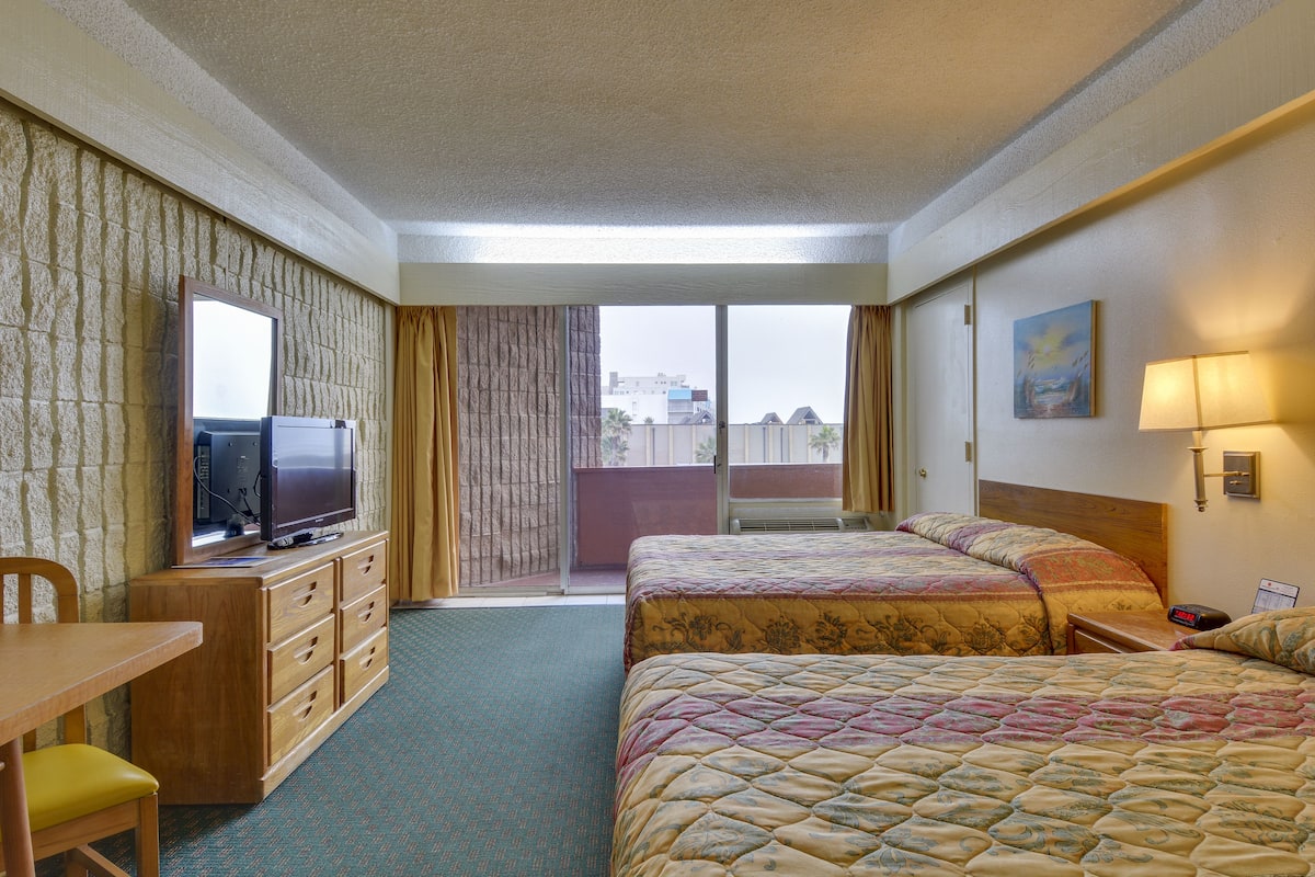 A hotel room with two beds, a desk, a television, and a view of the city through the window.