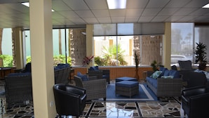Un hall con mobiliario de mimbre, suelo de baldosas y ventanas amplias.