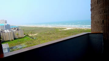 Vista desde un balcón sobre una playa, con un edificio al frente.