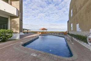 Ein Swimmingpool mit Sonnenschirm, umgeben von einer Ziegelterrasse und einem Gebäude mit weißer Fassade.