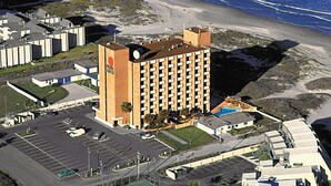 Un hotel de gran altura con una torre central y varios balcones, situado cerca de una playa donde las olas rompen en la orilla.