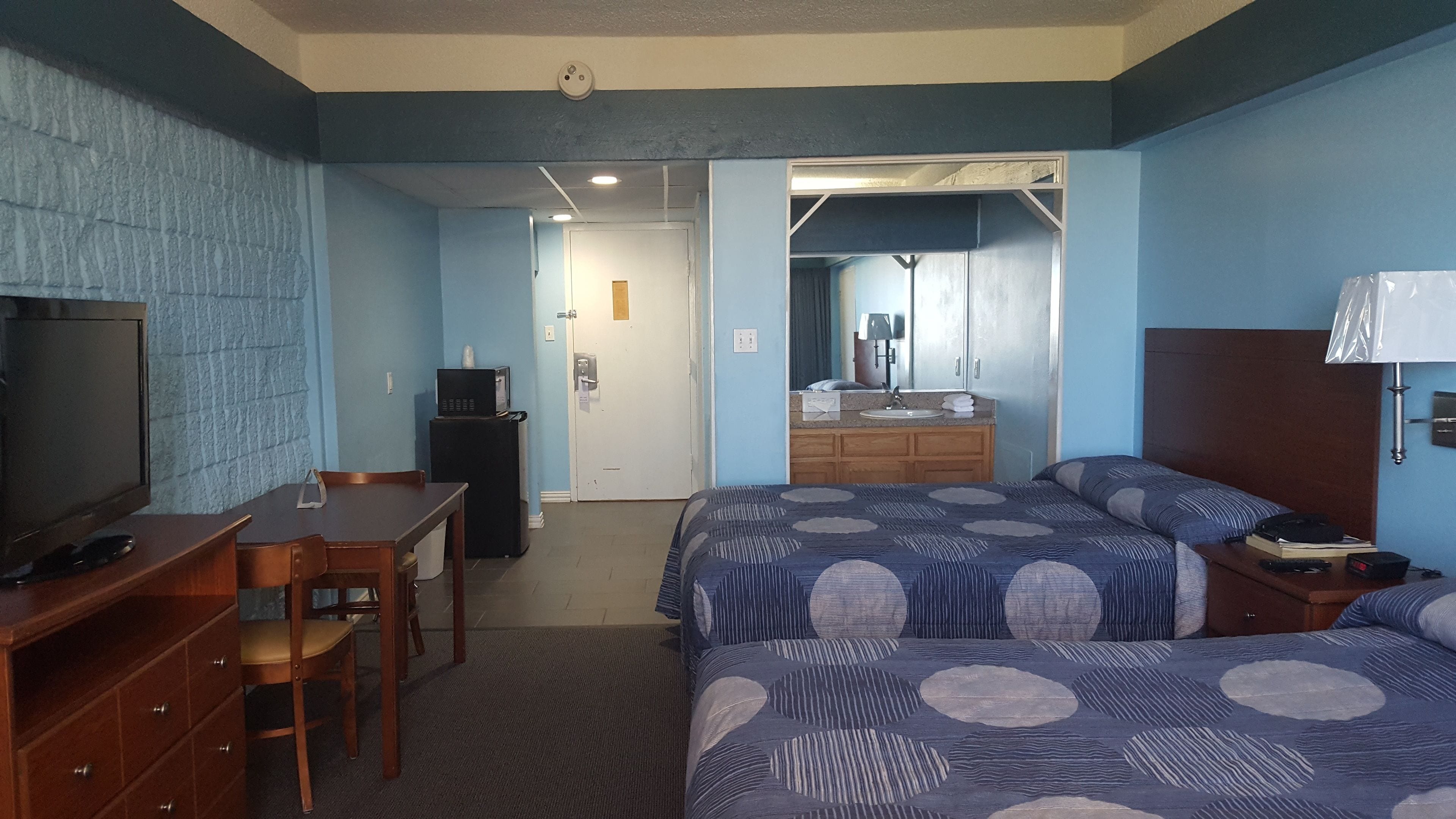 Une chambre d’hôtel avec un lit, un bureau, une télévision et une salle de bain visible à travers une porte ouverte.