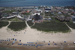 An aerial view of a coastal area with a beach, buildings, and a bridge in the background.
