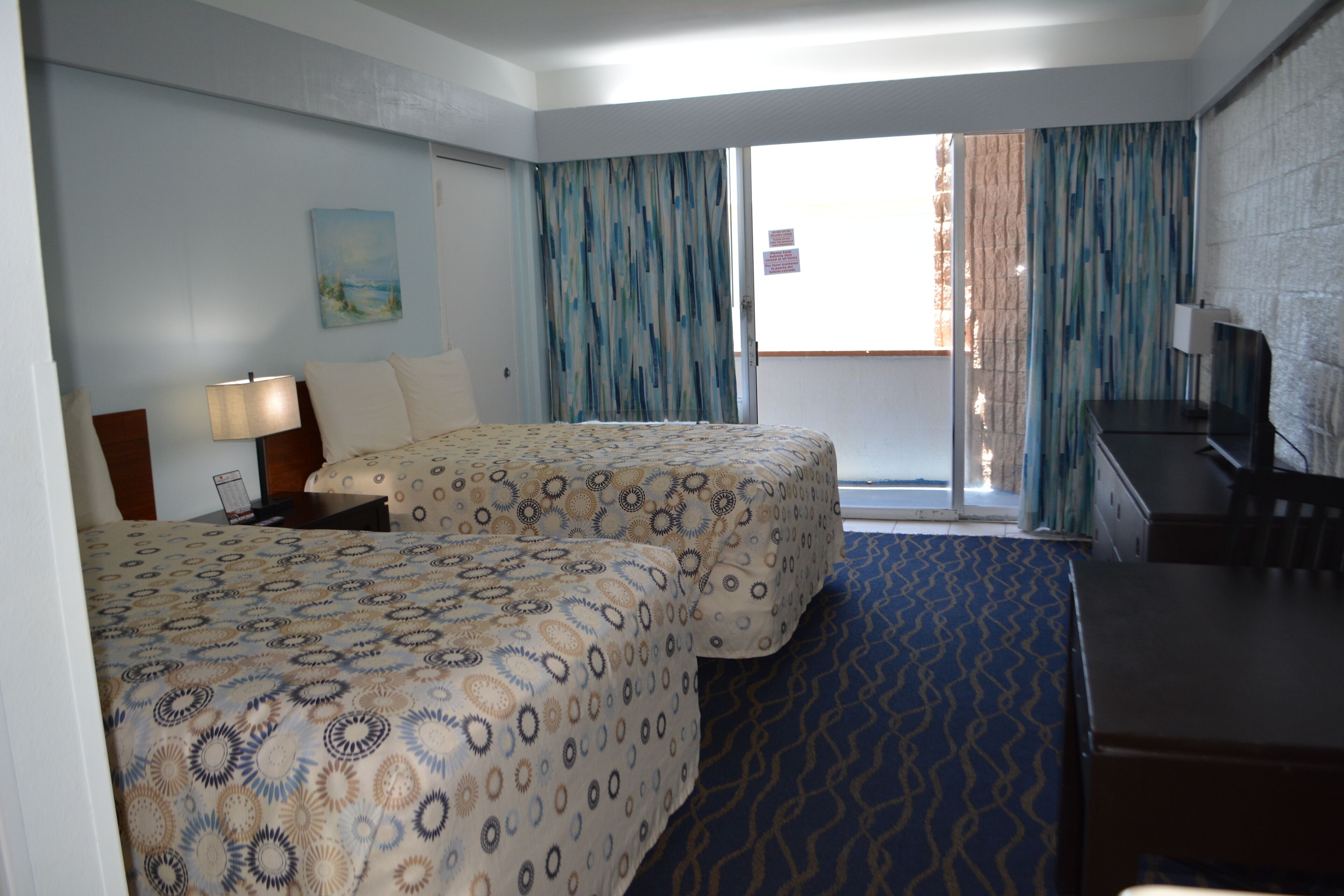 A hotel room with two beds, a desk, a chair, a TV, and a window with curtains.