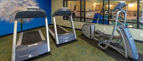 A fitness area with treadmills and a stationary bike, carpeted floor, and a large window with a view of a pool.