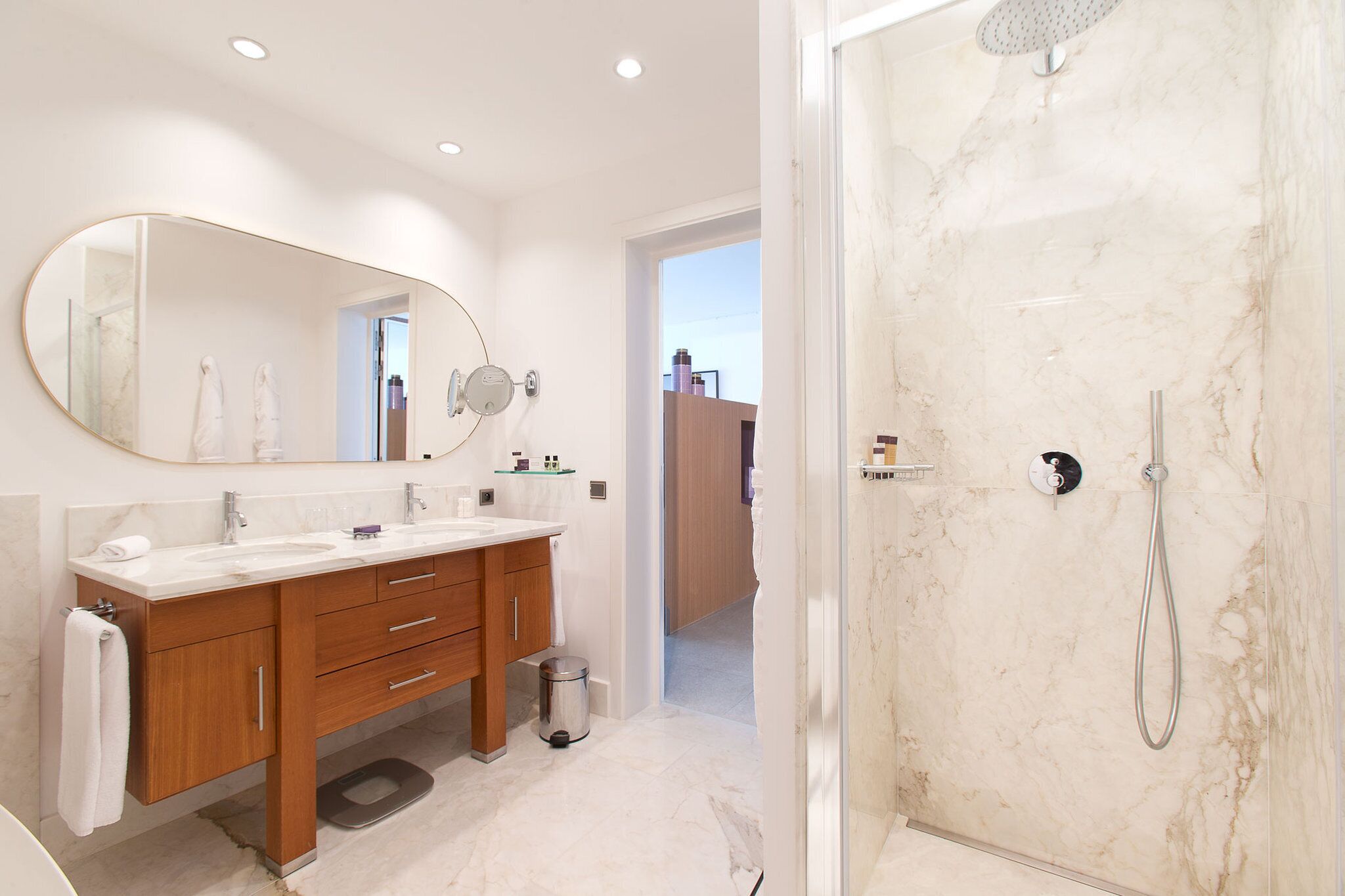 A modern bathroom with a double sink vanity, a large mirror, a shower with a handheld showerhead, and a marble floor.