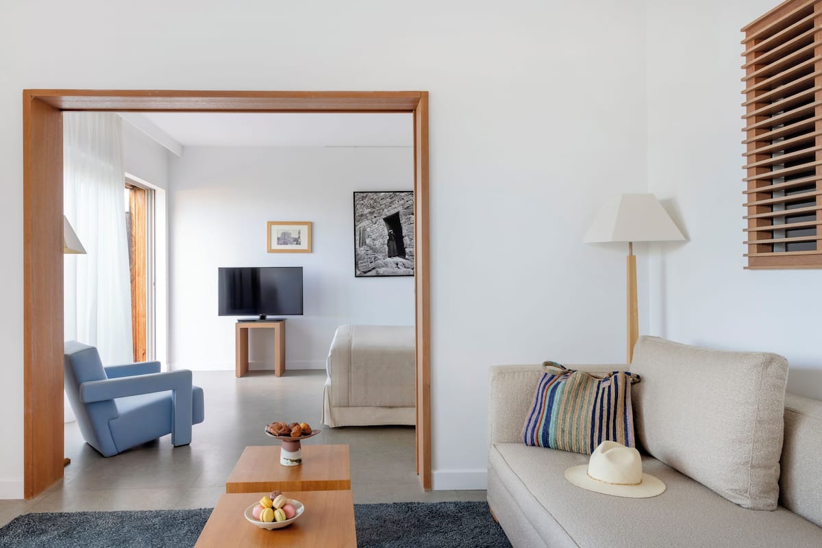 A modern living room with a sofa, a blue armchair, a coffee table with a bowl of fruit, a television, and a framed picture on the wall.