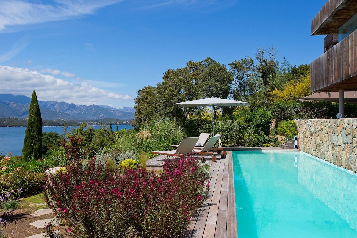 A pool with a wooden deck, lounge chairs, and an umbrella.