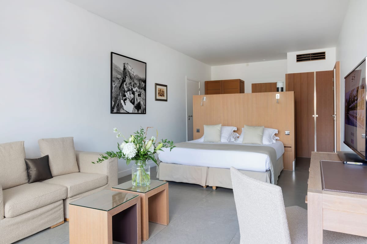 A modern hotel room with a bed, a sofa, a TV, and a coffee machine.