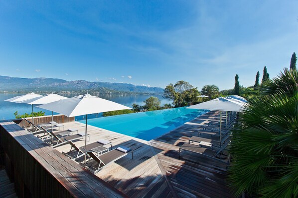 Terraza de madera con sillones y sombrillas con vista a una piscina y un lago.