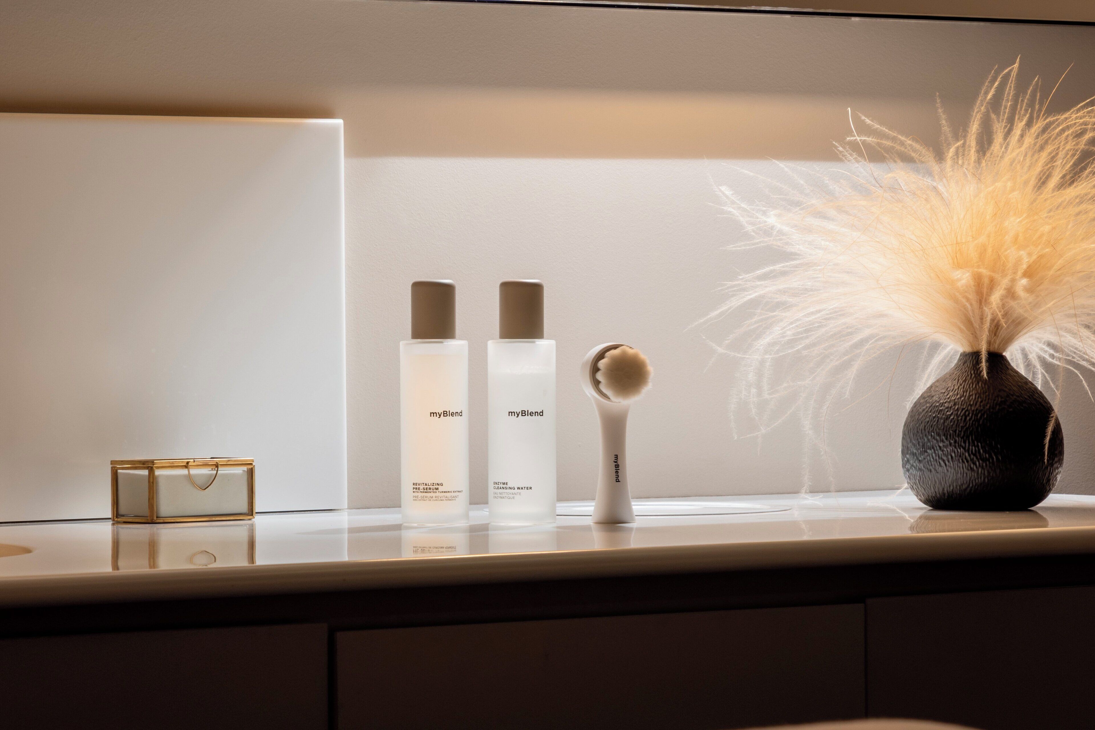 Un meuble-lavabo de salle de bain avec un miroir, un petit récipient rectangulaire et trois flacons de produits de soins pour la peau.