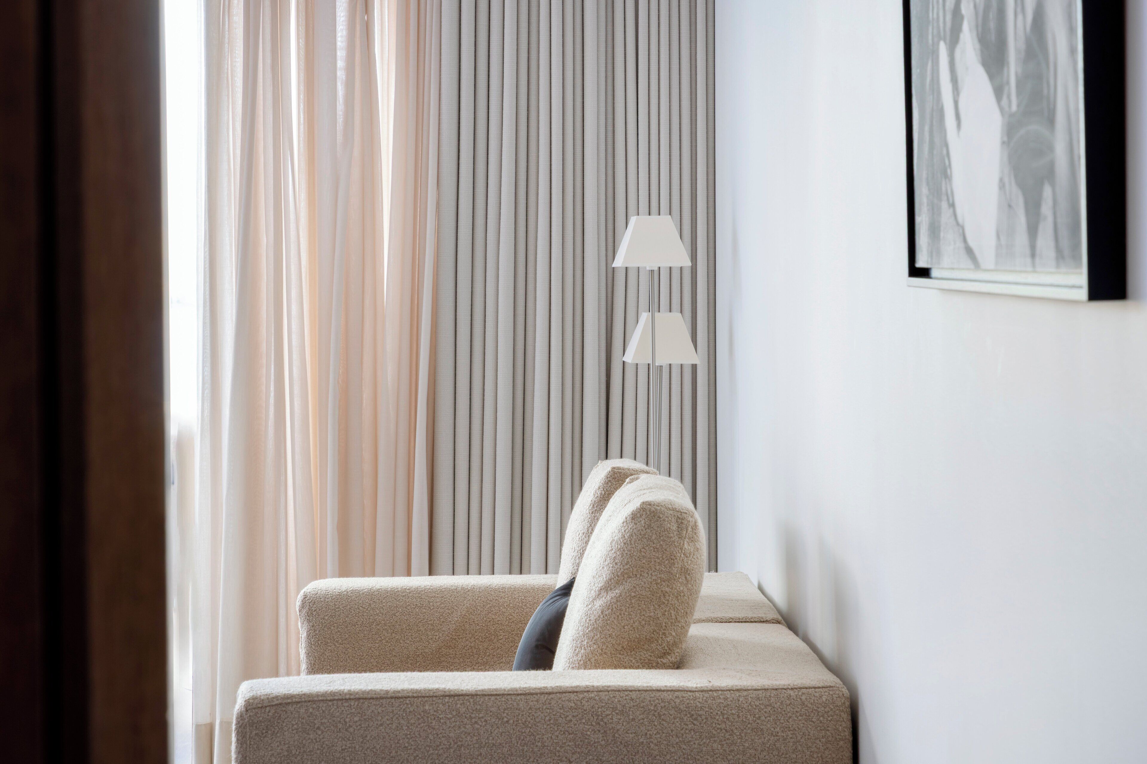 Une pièce moderne avec un canapé beige, un lampadaire et un rideau à rayures verticales.