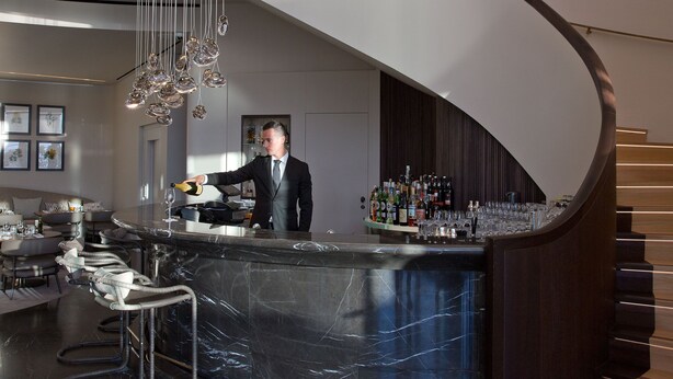 A modern bar area with a curved marble countertop, bar stools, and a bartender. - Casadelmar (Porto-Vecchio)