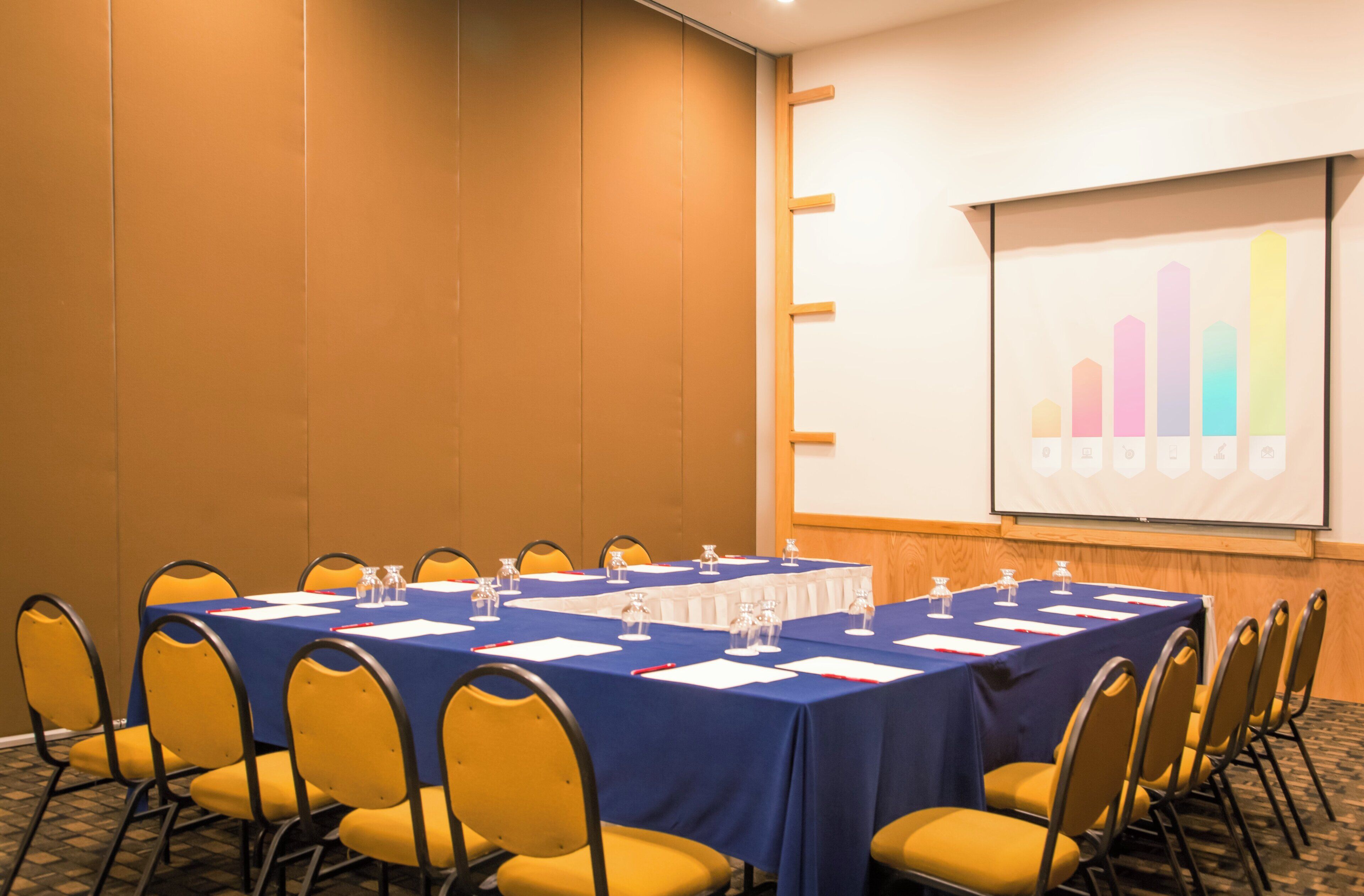 Una sala de conferències amb una taula llarga, cadires grogues i una pantalla que mostra un gràfic de barres.