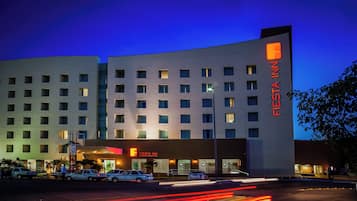 A multi-story hotel with a prominent 'Fiesta Inn' sign, featuring a modern architectural design with a flat facade and evenly spaced windows.