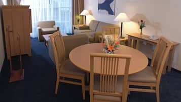 Une chambre d’hôtel avec une table de salle à manger ronde, quatre chaises en bois, un canapé, un bureau avec une lampe, un téléphone et un vase rempli de fleurs.